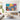 Framed horizontal folk art oil painting bringing tropical storybook warmth and vivid colors above a light wooden console in a living room.