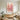 Hand-painted colorful petal artwork in a light wood frame on a hallway wall above a slim console table with a small lamp and woven basket