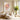 Large hand-painted bouquet canvas with golden yellow and lavender brushwork on a warm white living room wall beside a rattan chair and plant