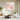 Framed square pink flower canvas artwork bringing delicate spring wind vibes above a light wooden sideboard in a serene living room setup.
