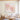 Hand painted pink sakura blossom square oil painting with light knife texture hanging over a beige sofa in a sunlit modern living room.