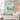 Framed square ocean blue floral canvas artwork bringing cool refreshing water vibes above a light wooden console in a contemporary home.