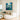 Hand painted deep teal abstract floral square oil painting with gold frame hanging over a grey sofa in an elegant moody living room.