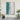 Large vertical aerial beach canvas painting with turquoise sea foam displayed in a minimalist hallway next to indoor potted green plants.
