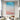Vertical coastal ocean canvas artwork hanging above a white sectional couch in a high-ceiling modern room.